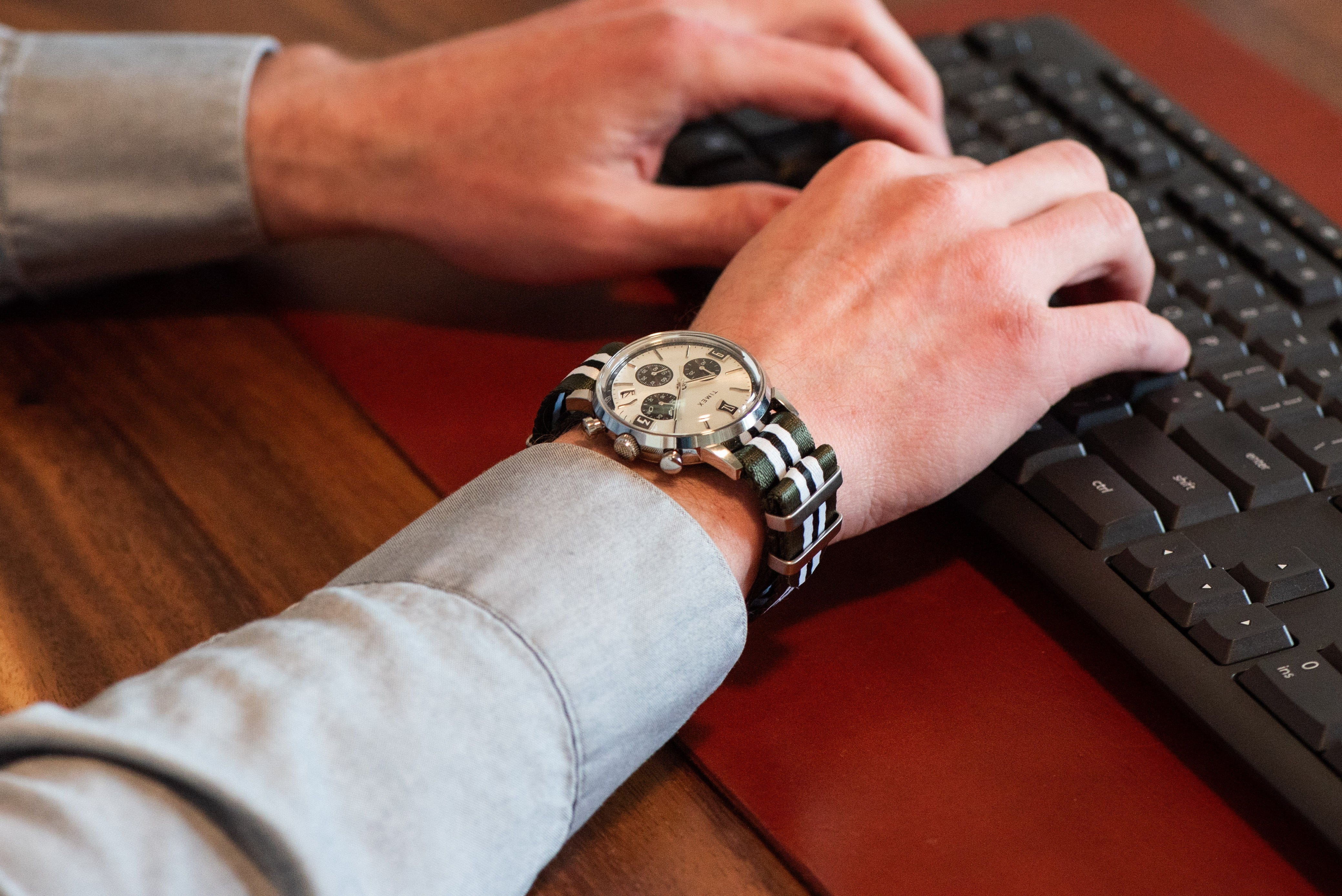 Person typing on a keyboard with a watch on their wrist, sitting at a wooden desk. Nylon military Style watch strap 