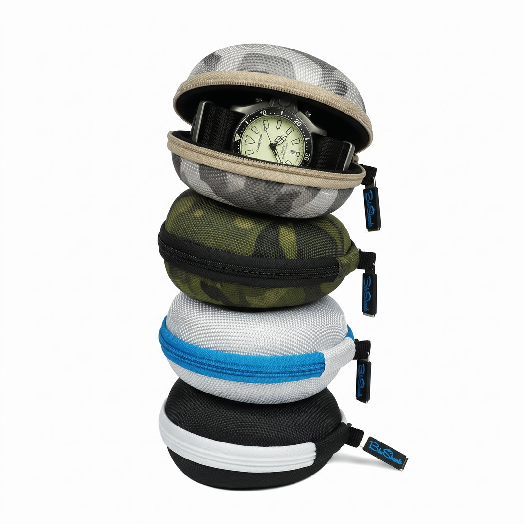Four round zippered watch storage cases stacked vertically on a white background, with a watch partially visible inside the top case. The cases come in camouflage and solid color options: gray and black camo, olive green camo, white and green camo, and black and white.
